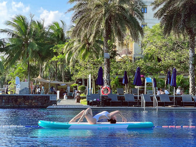 Turquoise paddleboard with a woman doing yoga.